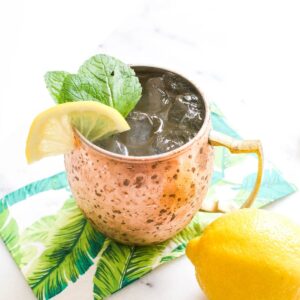 Lemonade mule on top of a tropical patterned napkin with a whole lemon to the side.