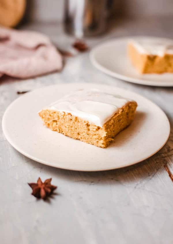 White plates holding square pieces of pumpkin cake on them with fabric napkin and spices on a table.