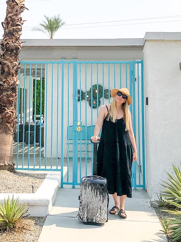 A girl in black dress with a suitcase in front of a vacation property in Palm Springs.