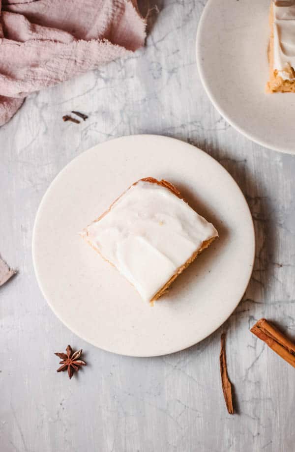 Square piece of pumpkin spice cake on a dessert plate with spices and napkin on the table next to it.