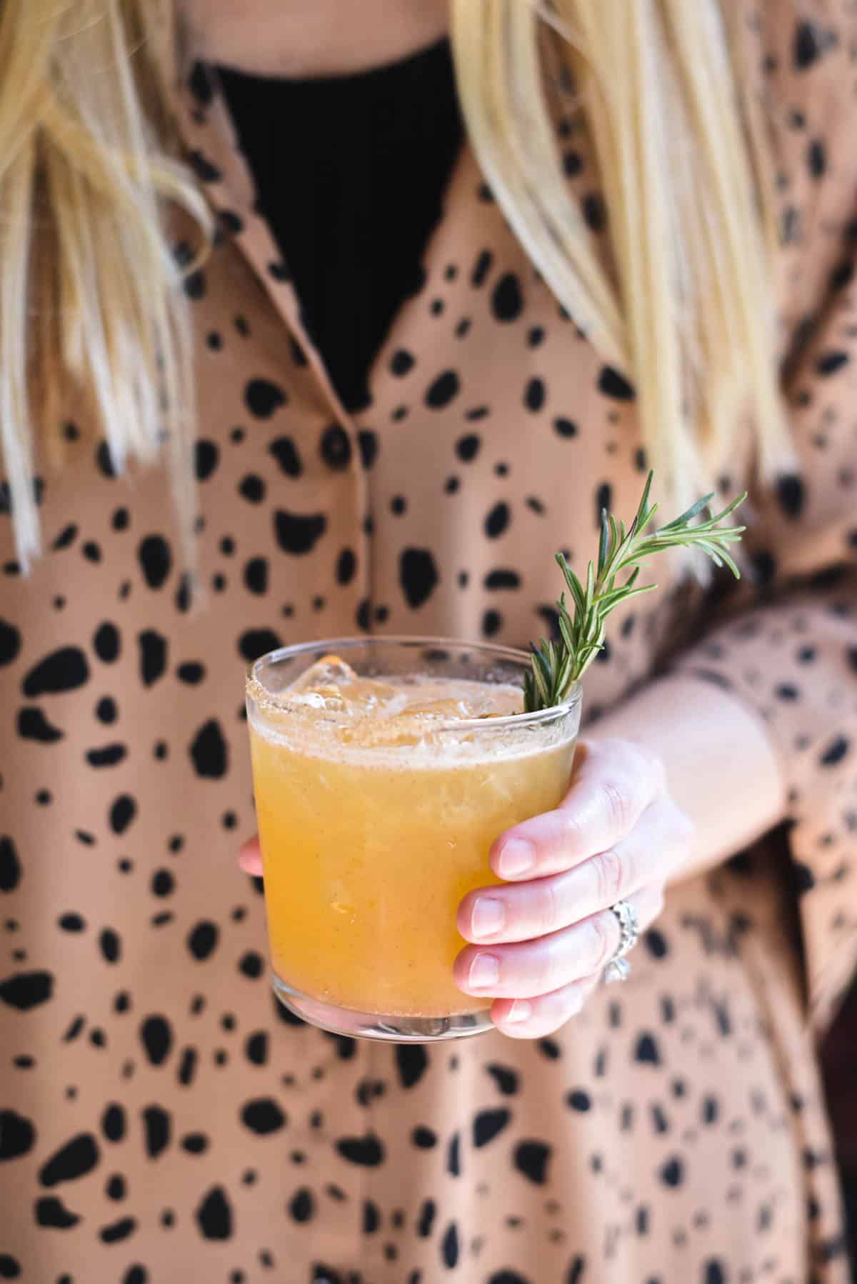 Woman holding a cocktail in her hand with rosemary sprig garnish.