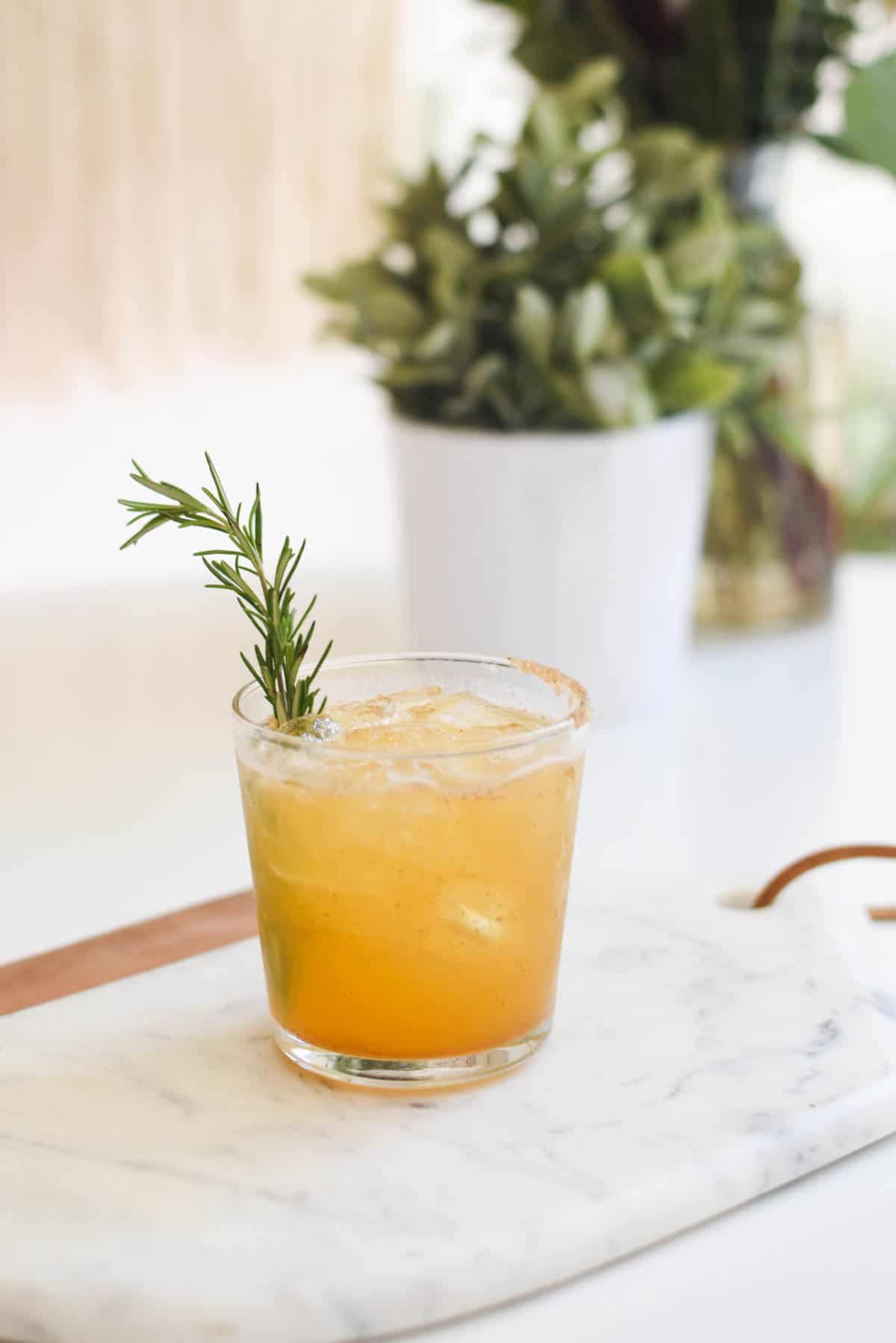 Cocktail on a table with rosemary sprig garnish.
