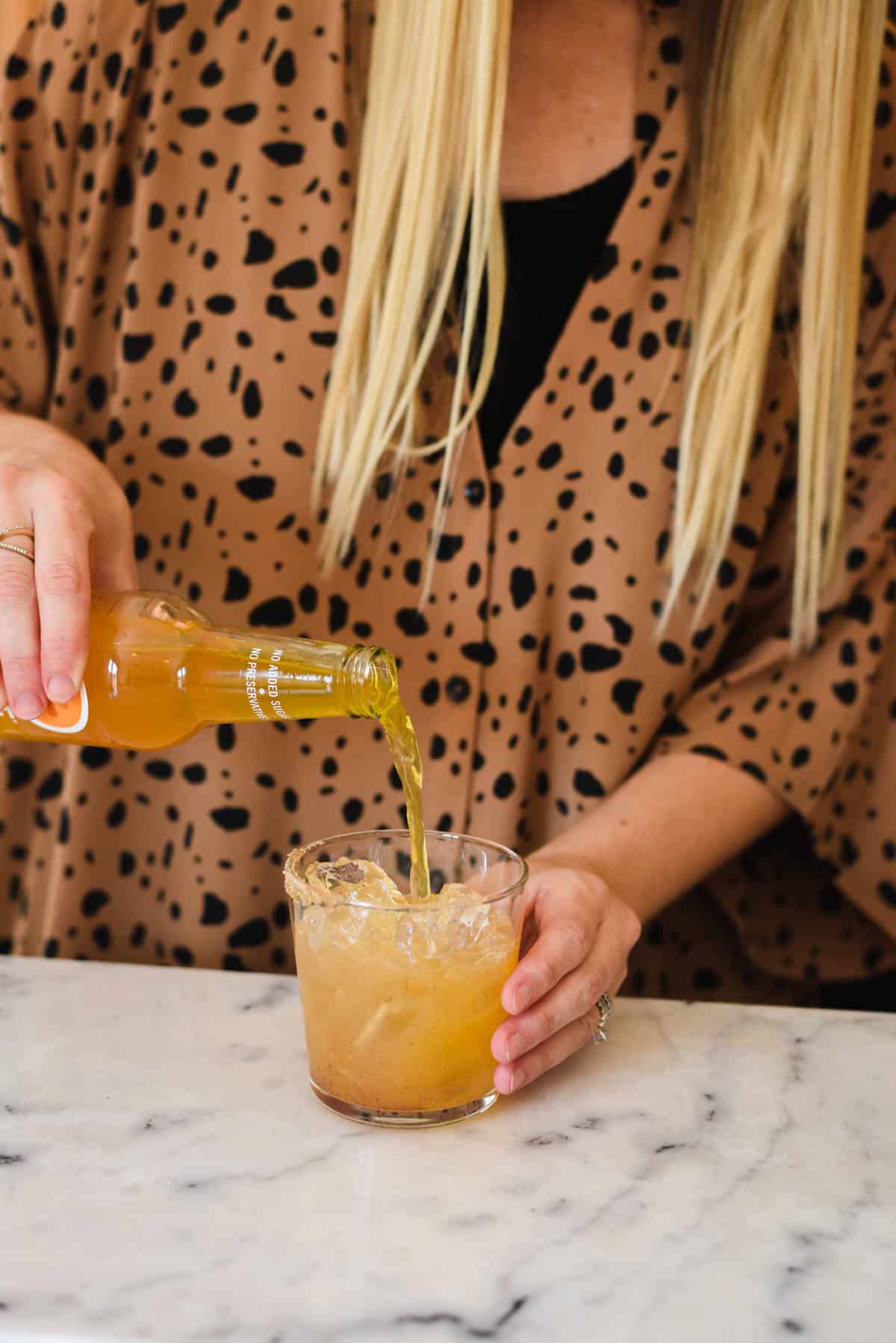 Woman pouring Clementine Izze Soda over ice into a cocktail glass.