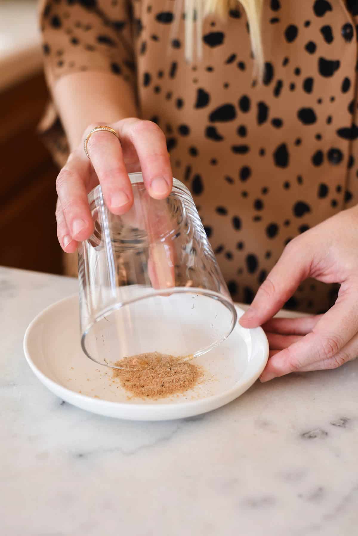 Woman dipping a cocktail glass in spiced sugar on a small plate.