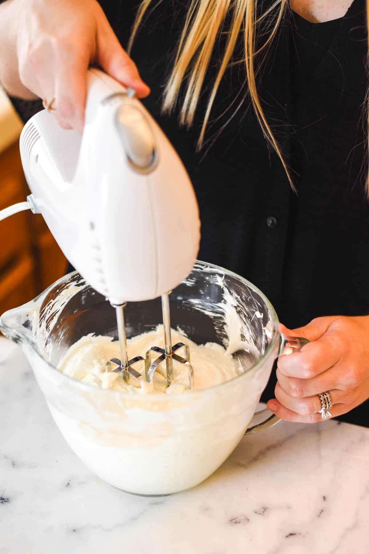 Woman using a hand mixer to mix up a cream cheese mixer.