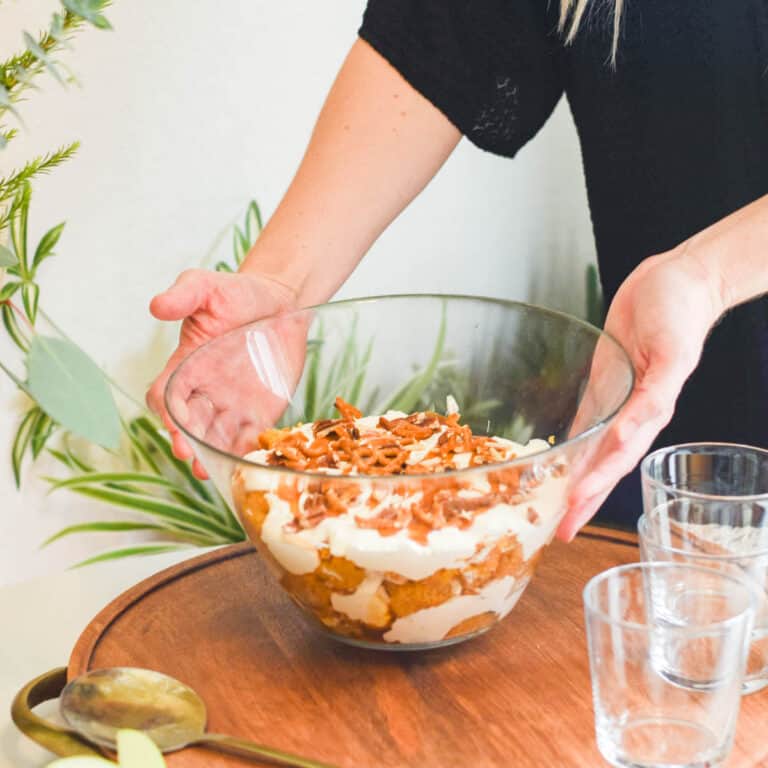 Woman placing a pumpkin trifle dessert on a holiday party table.
