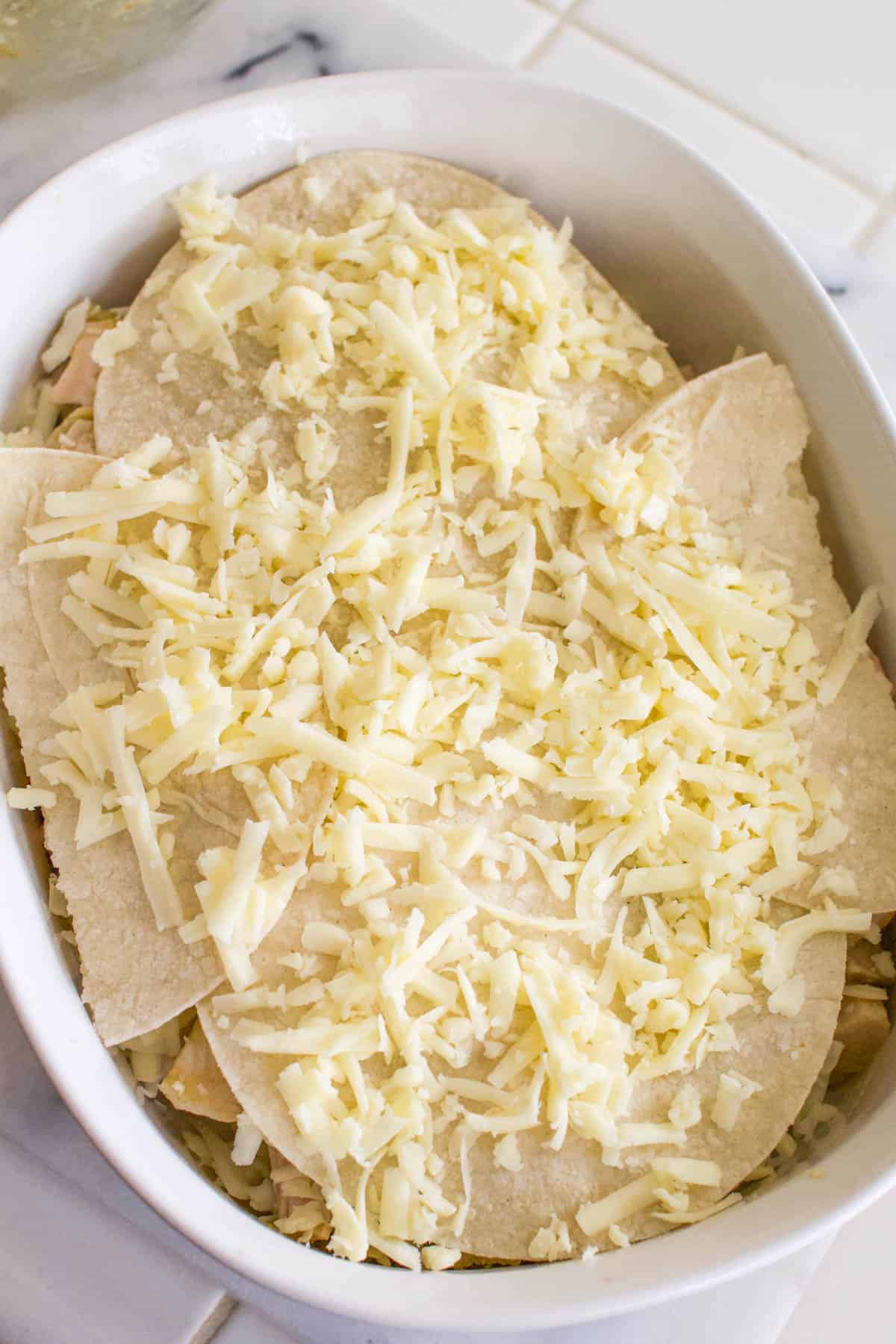 Baking dish with layered chicken, cheese and tortilla for a casserole.