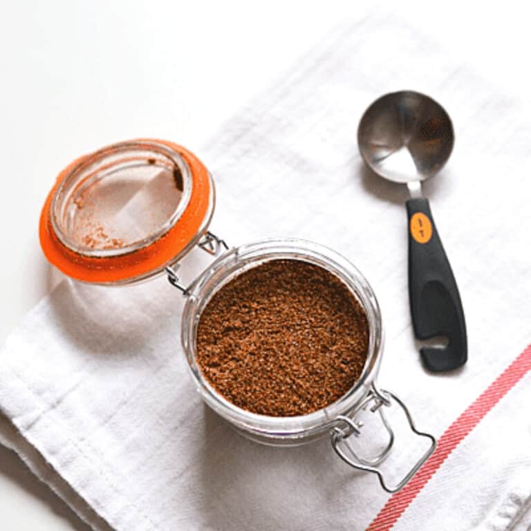 Glass canister with seasoning on a table next to a measuring spoon.