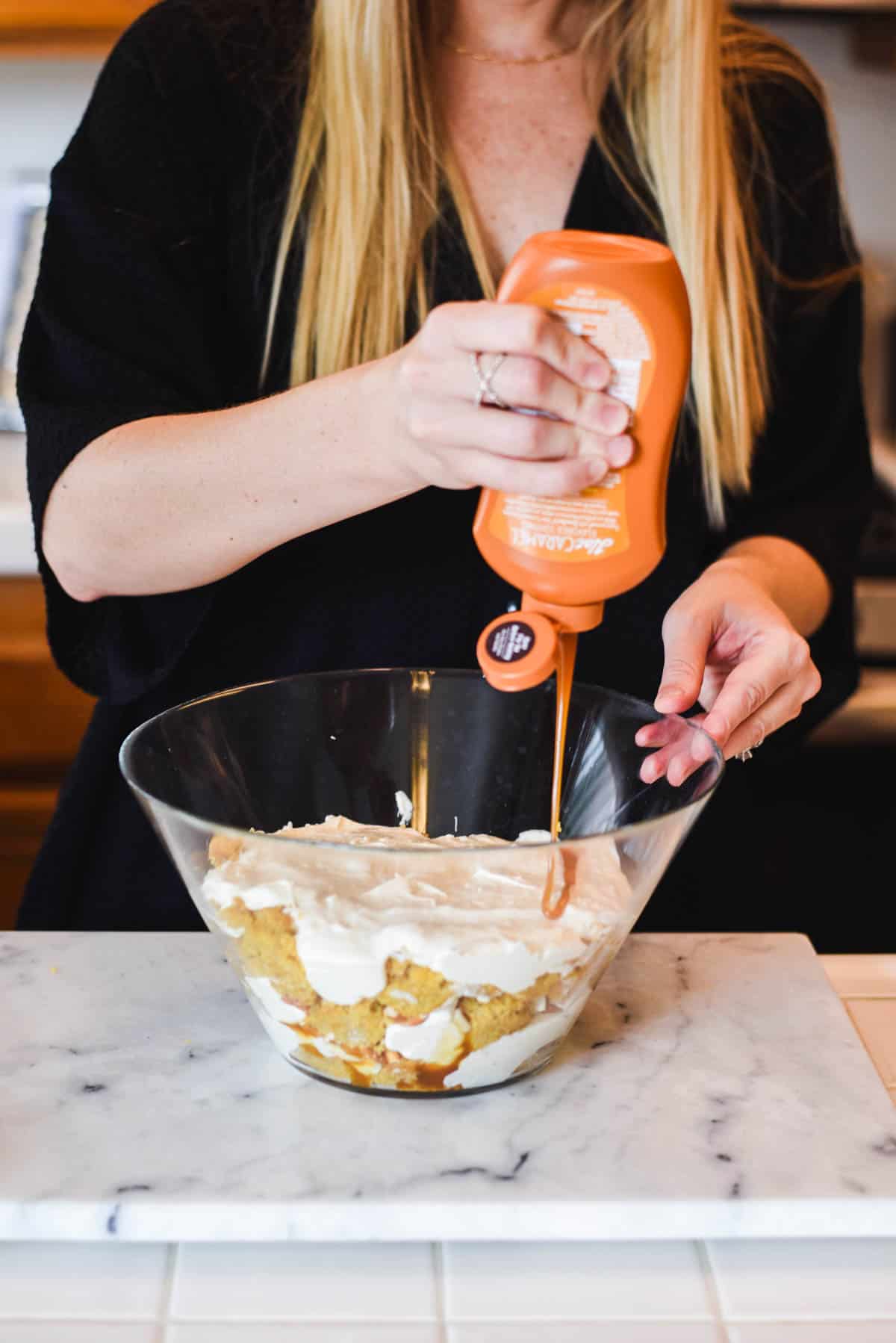 Woman adding caramel to the top of a layered dessert.