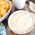 Bowl of cold bacon dip on a tray next to a bowl of potato chips.