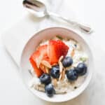 Overhead view of a bowl with chilled Swiss Oats topped with fresh strawberries, blueberries and almonds with a spoon next to it.