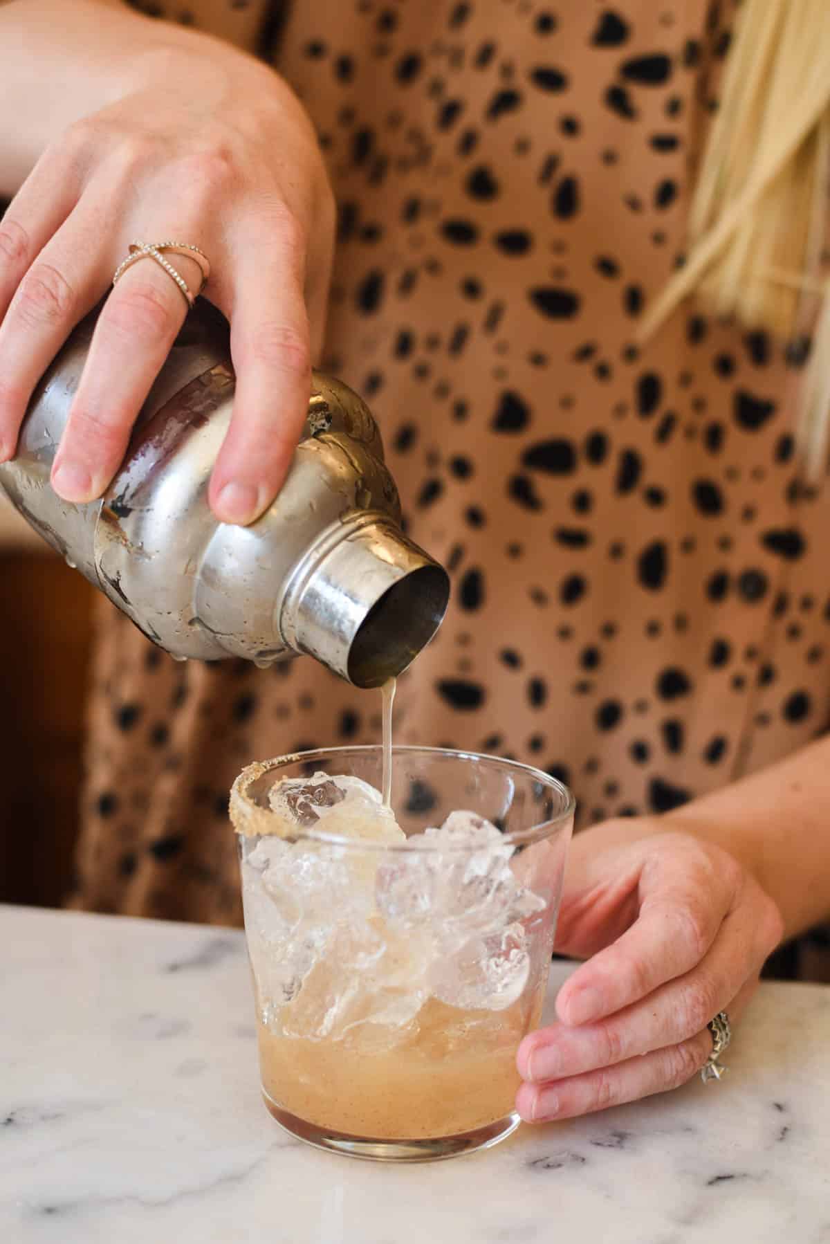 Woman pouring margarita into a cocktail glass filled with ice.