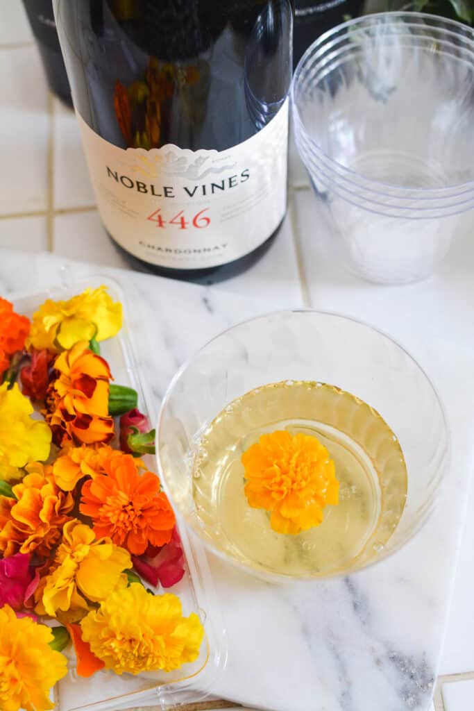 Edible flowers in a container next to a small glass of wine with one as garnish.