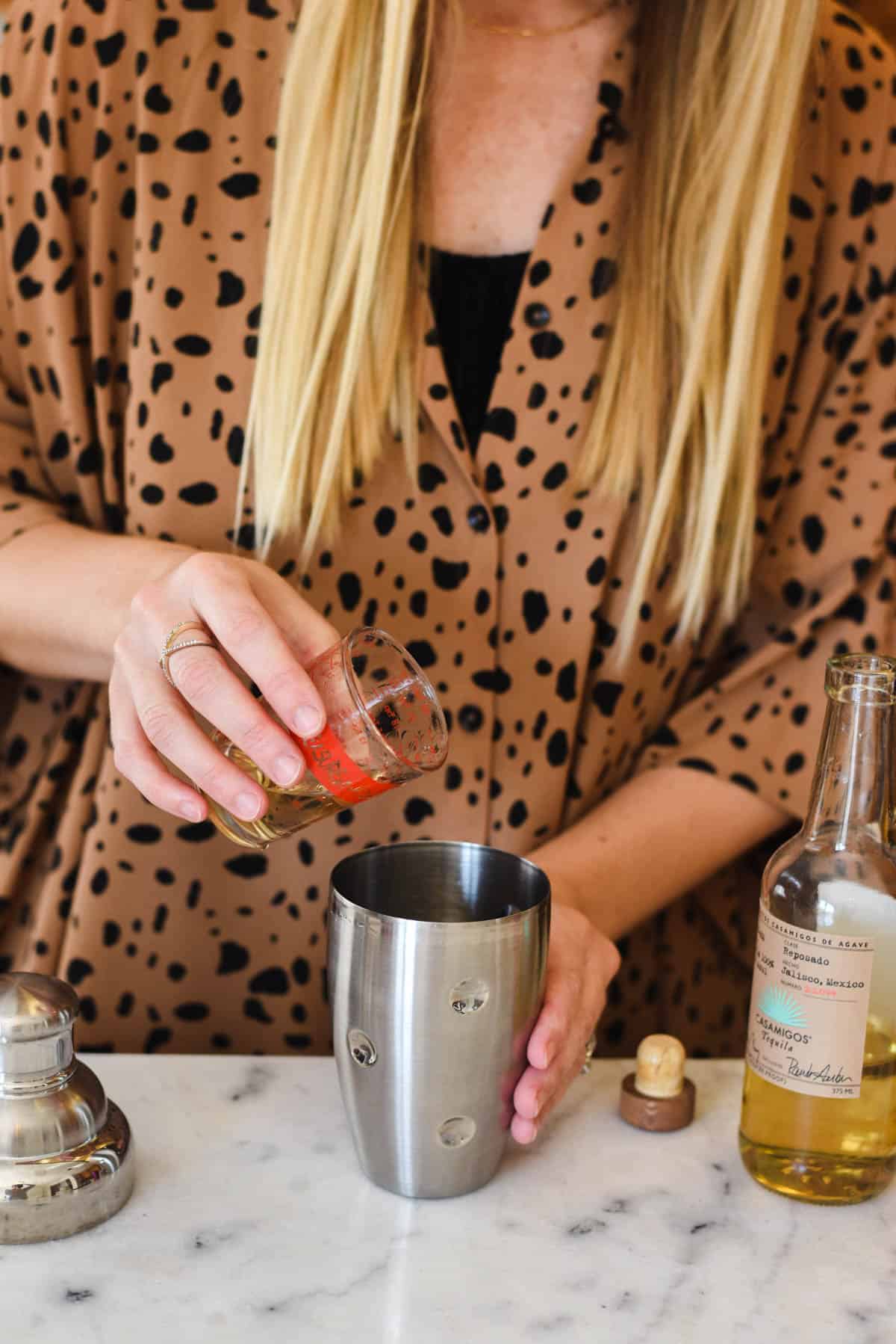 Woman adding tequila to a cocktail shaker.