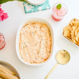 A baking dish with hot bacon dip next to a serving spoon and crackers.