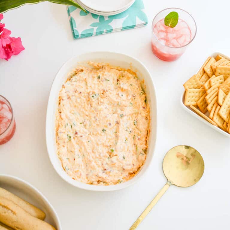 A baking dish with hot bacon dip next to a serving spoon and crackers.