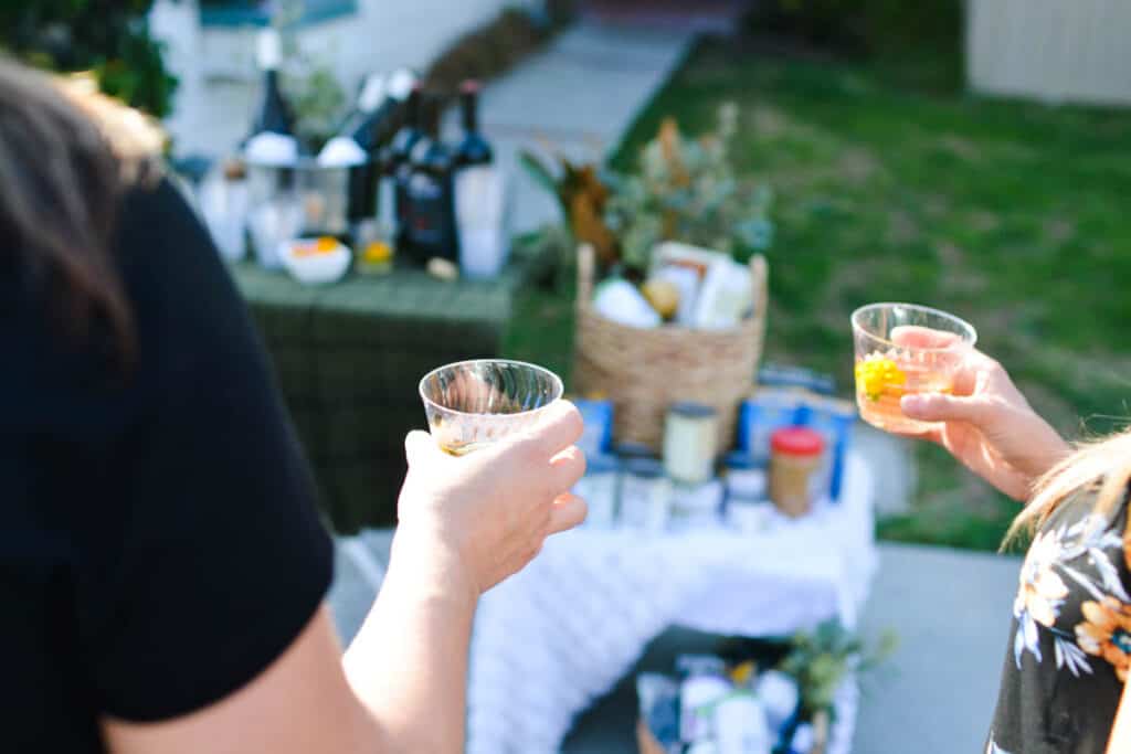 Two women holding small glasses of wine with a party table in the background.