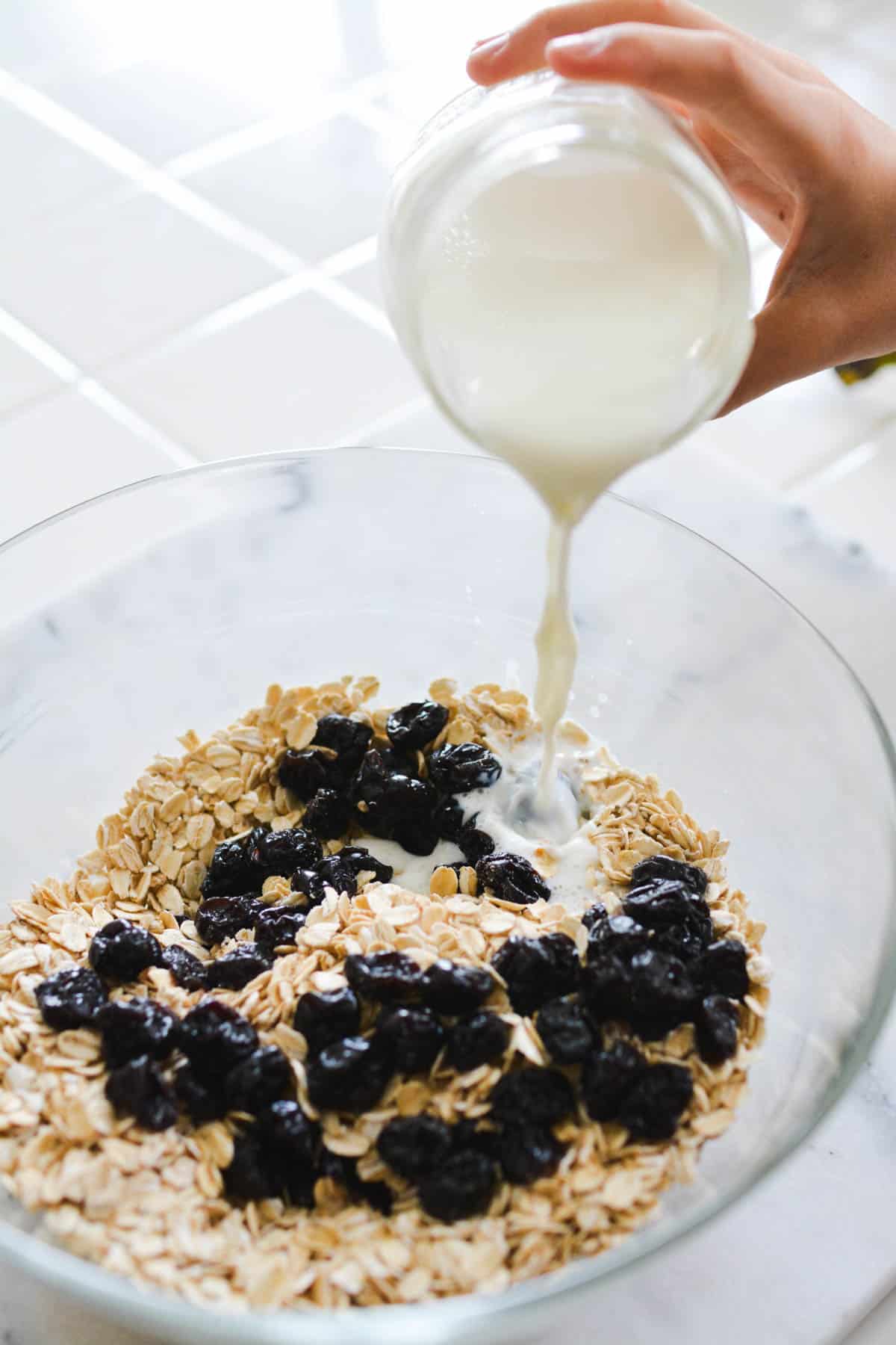 A bowl with oats and dried cherries and a kid pouring milk in.