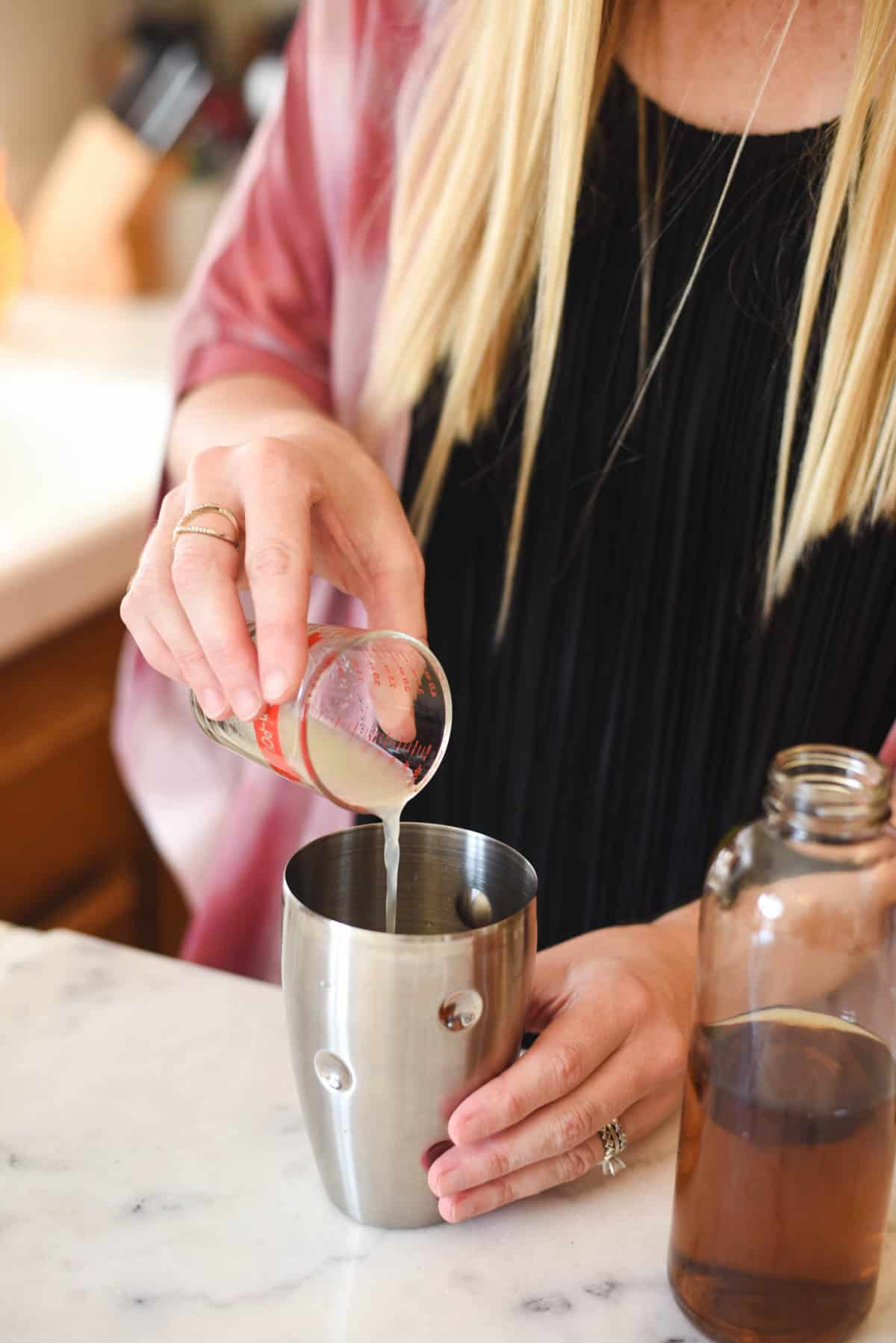 Woman adding fresh lime juice to a cocktail shaker.