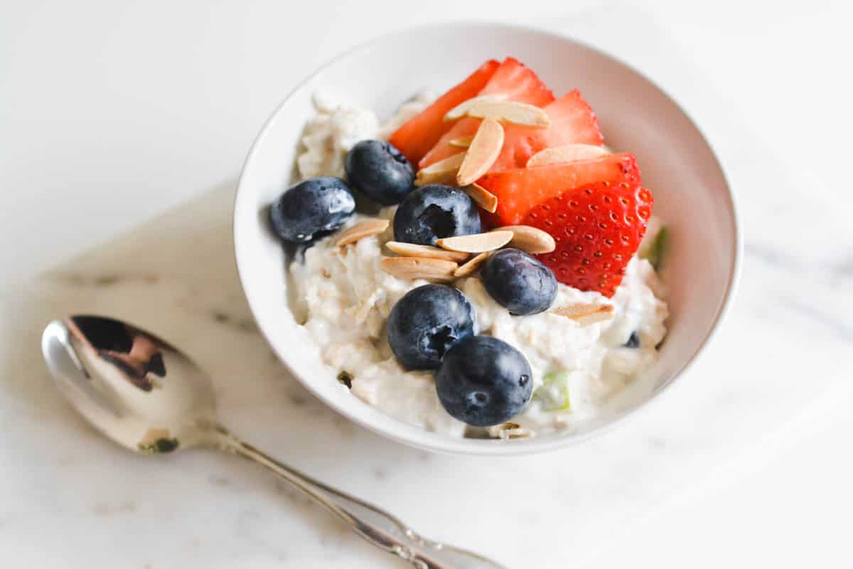 A small bowl of chilled oats on a cutting board topped with fresh berries and almonds.