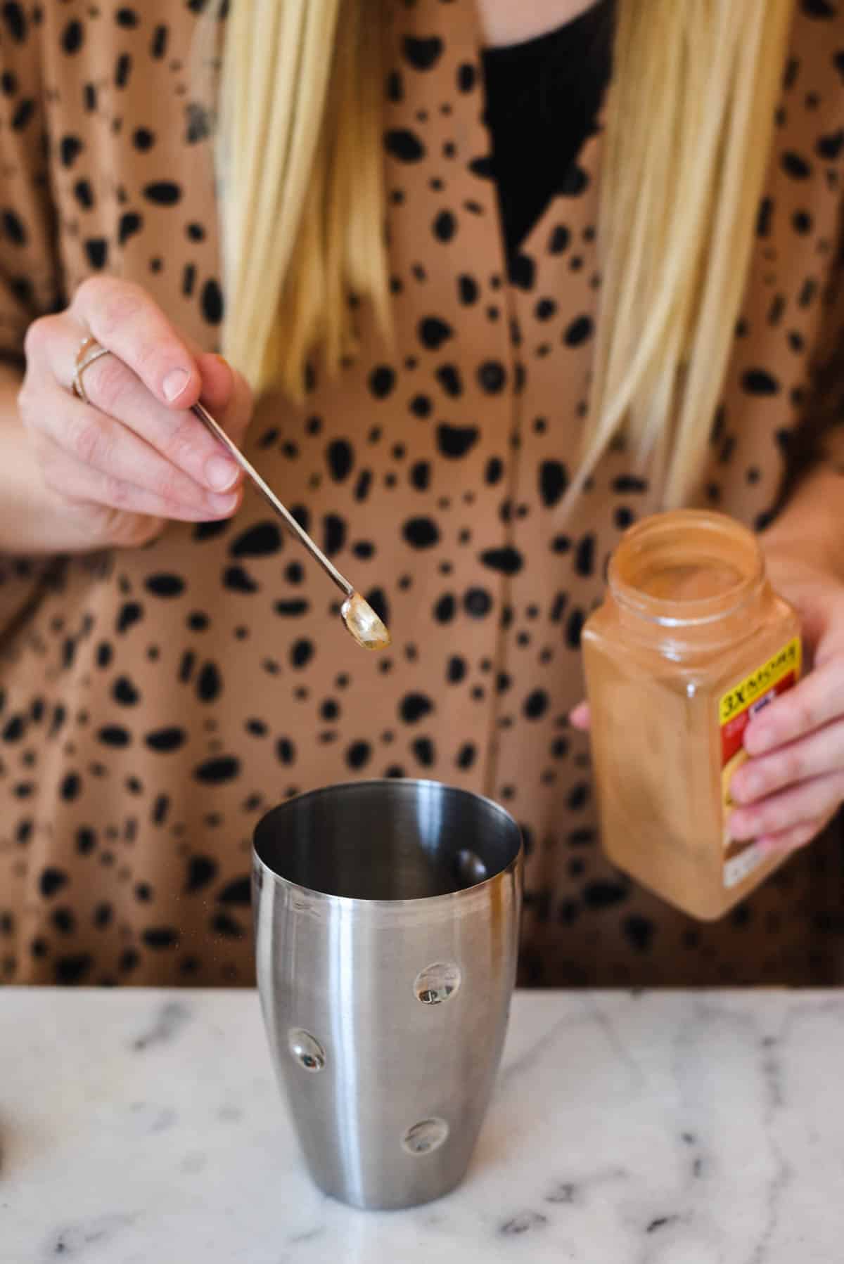 Woman adding cinnamon to a cocktail shaker.