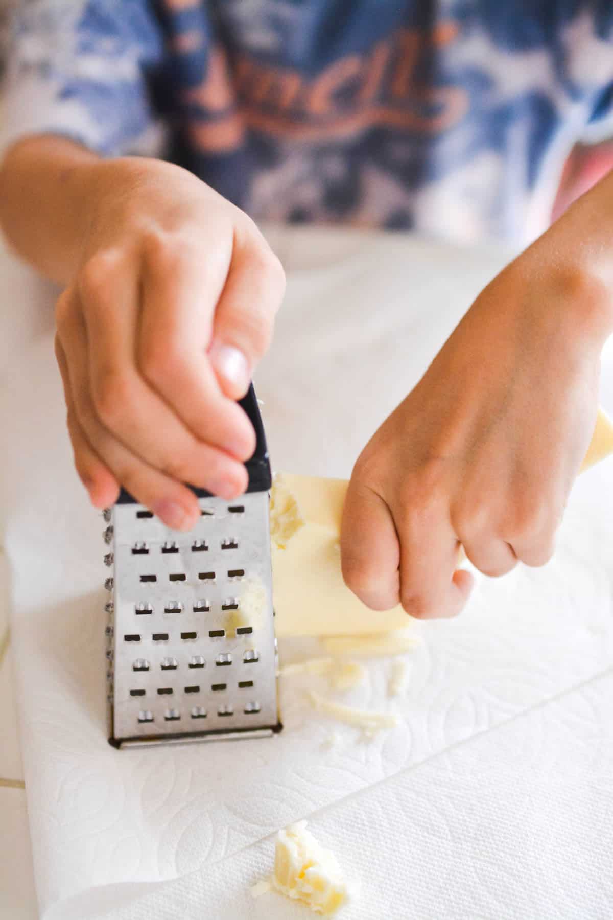 Kid grating swiss cheese at a kitchen counter.