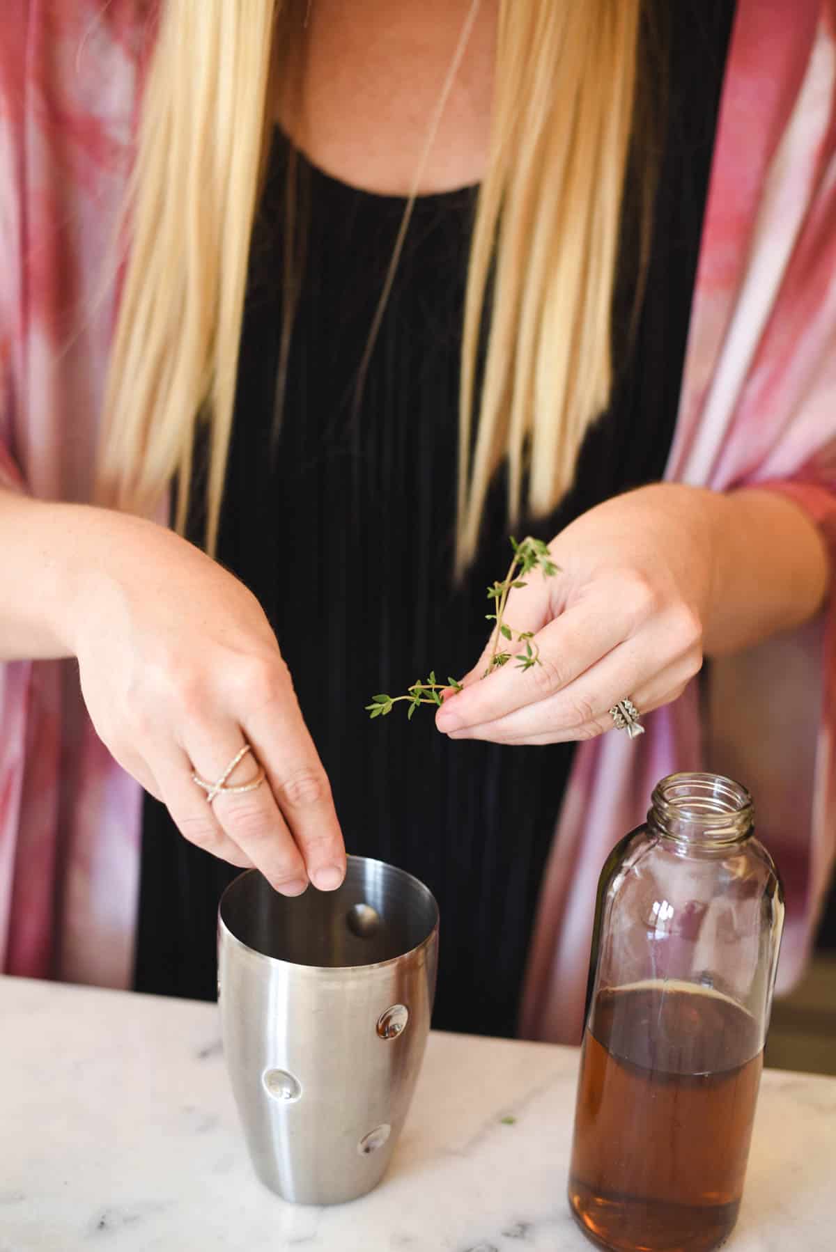 Woman putting fresh thyme in a cocktail shaker.
