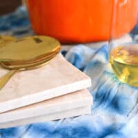 A stack of tile trivets on a table next to a dish and a glass of wine.
