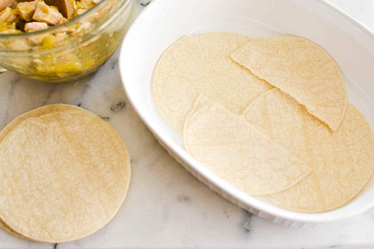 Casserole dish with tortilla lining the bottom and next to it on a counter. 
