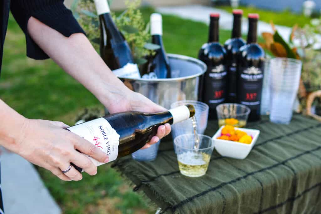 Woman pouring white wine in a glass on a drink table.