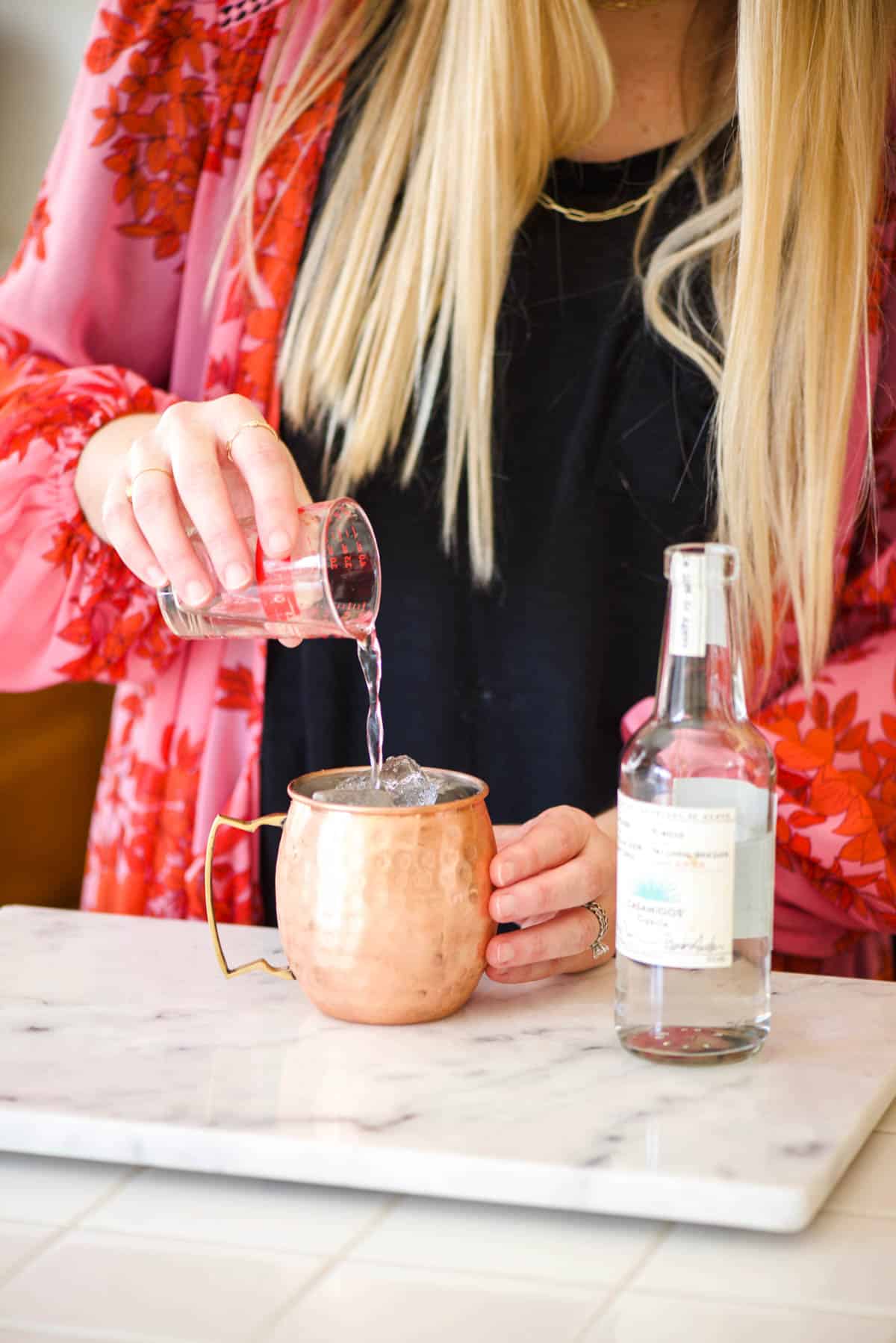 Woman adding tequila to a copper Moscow Mule mug.