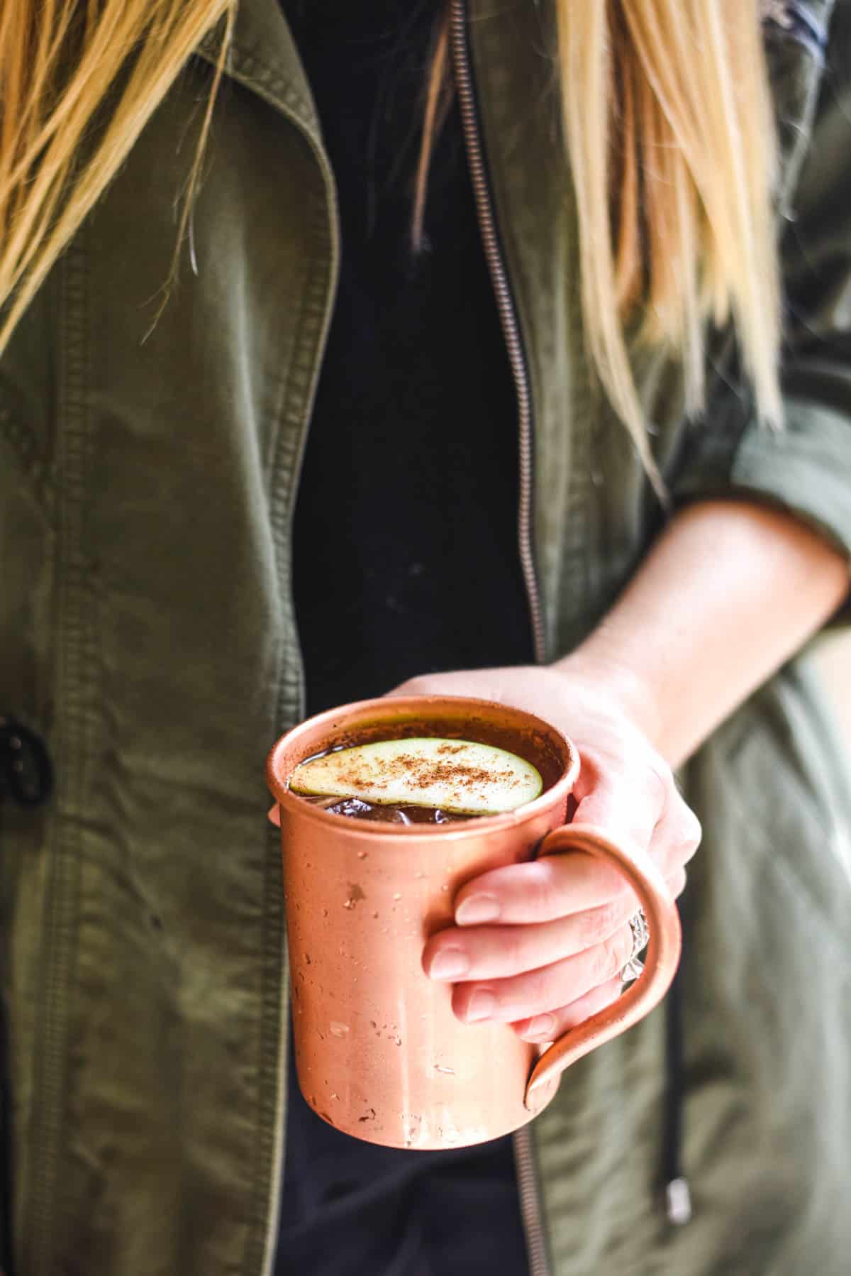 Woman holding a copper mug that is garnished with an apple slice.