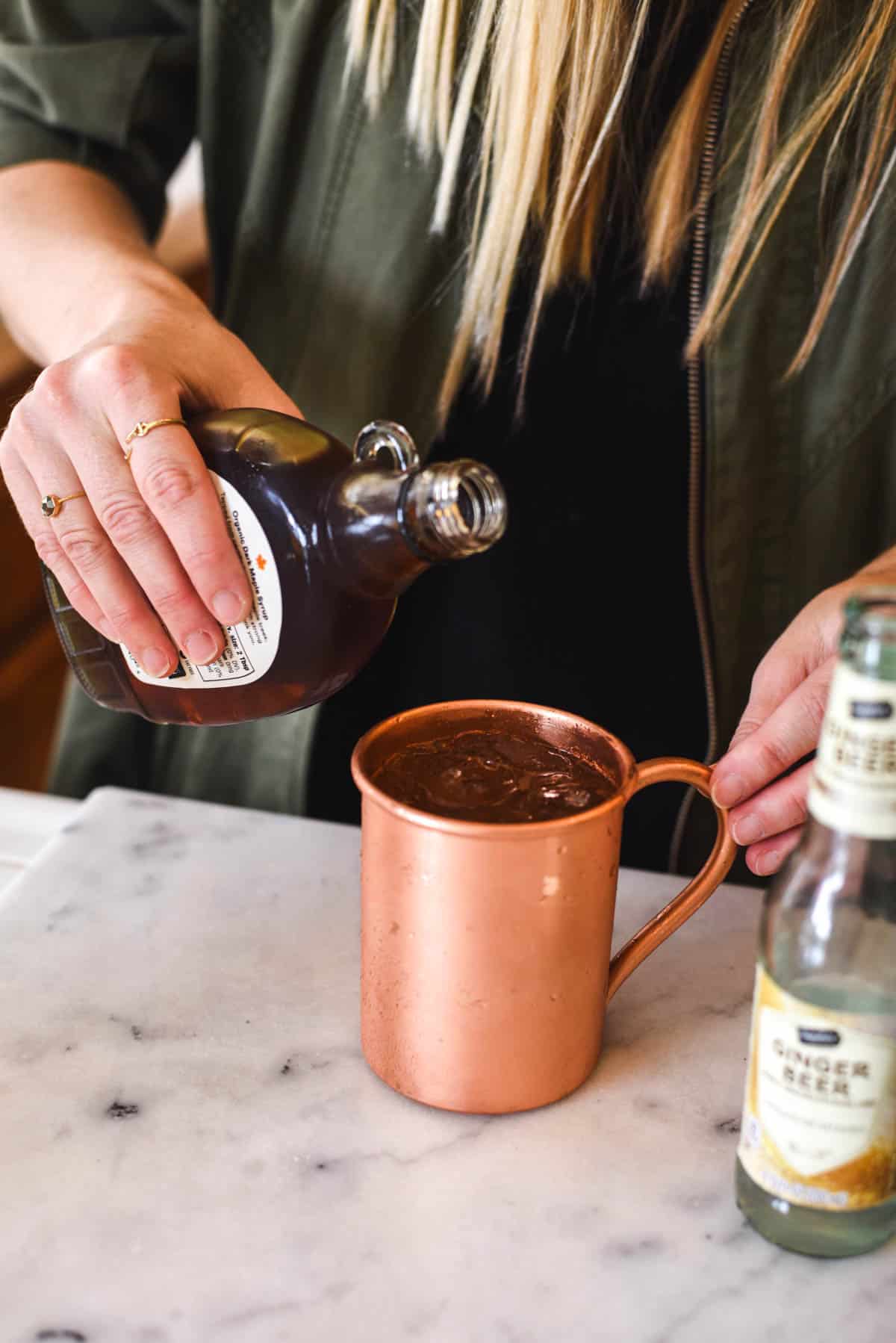 Woman adding maple syrup to a copper mug.