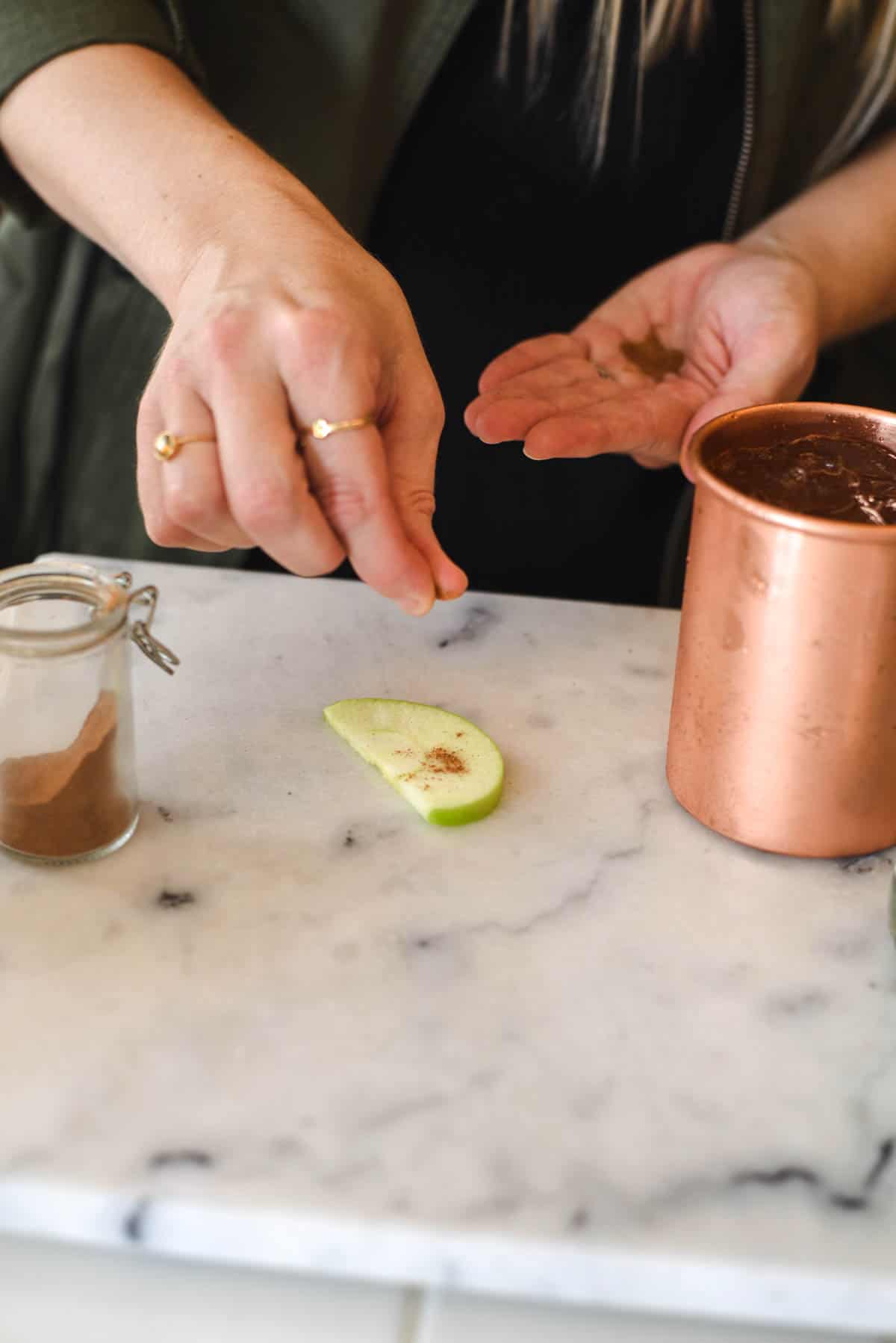 Woman adding a pinch of pumpkin pie spice to a slice of apple on a cutting board.