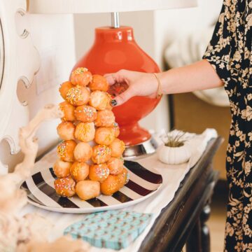 Woman taking a donut hole from a donut hole tower on a table.