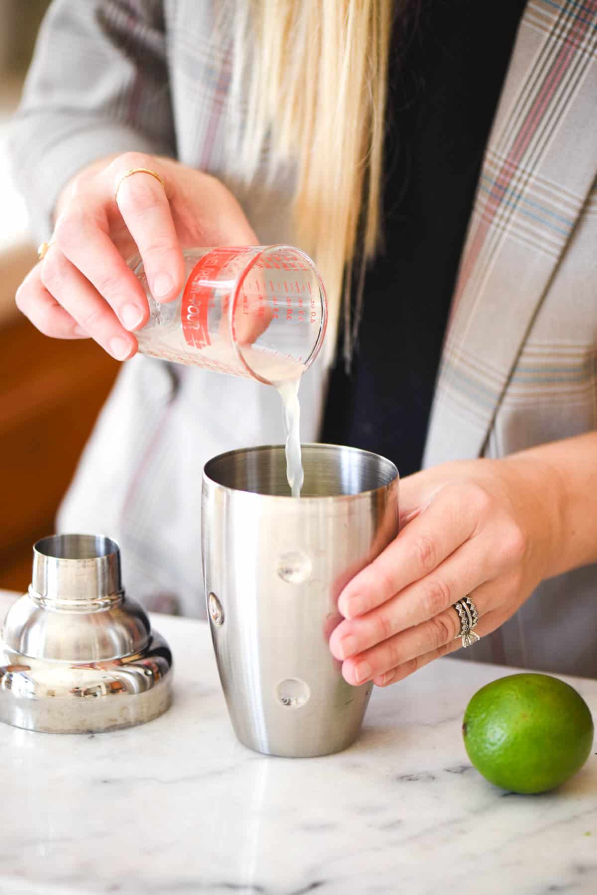 Woman pouring fresh lime juice in a cocktail shaker.