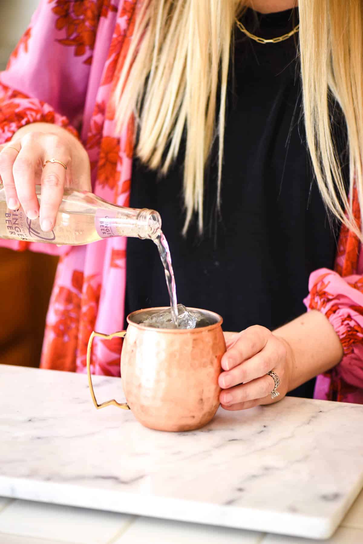 Woman pouring ginger beer into a copper mug.