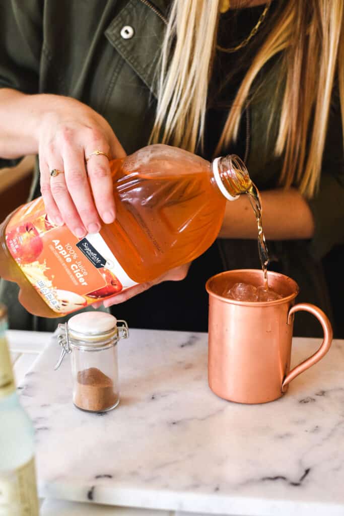 Woman pouring apple cider into a copper Moscow Mule mug.
