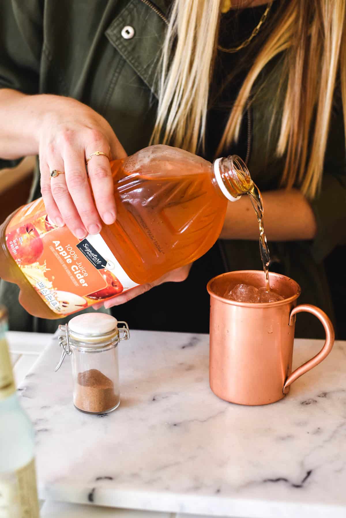 Woman pouring apple cider into a copper Moscow Mule mug.