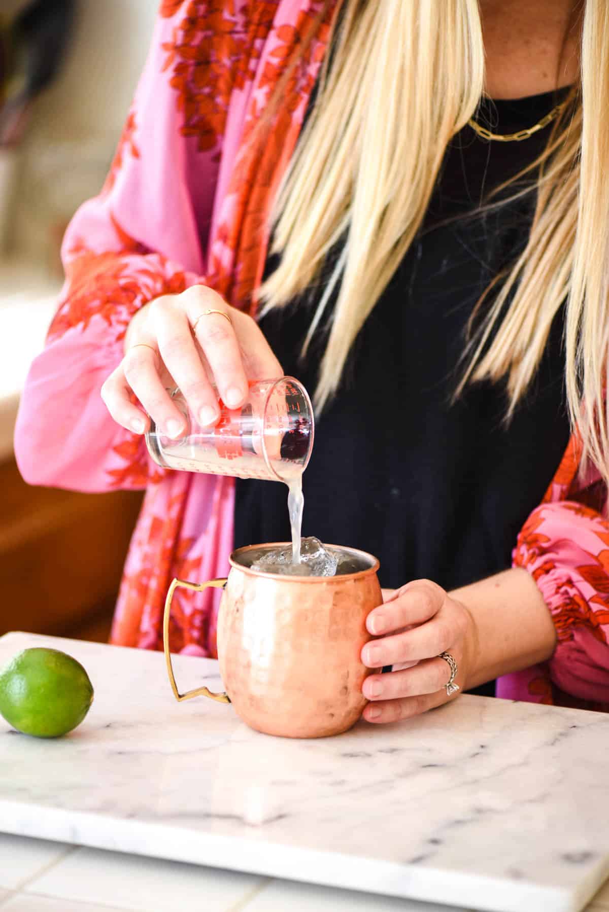 Woman pouring lime juice in a copper mug on a counter.