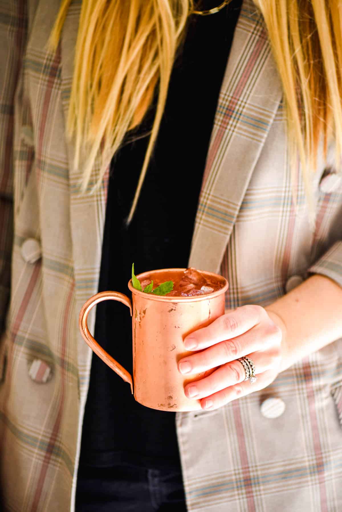 Woman holding a cocktail in a copper mug.