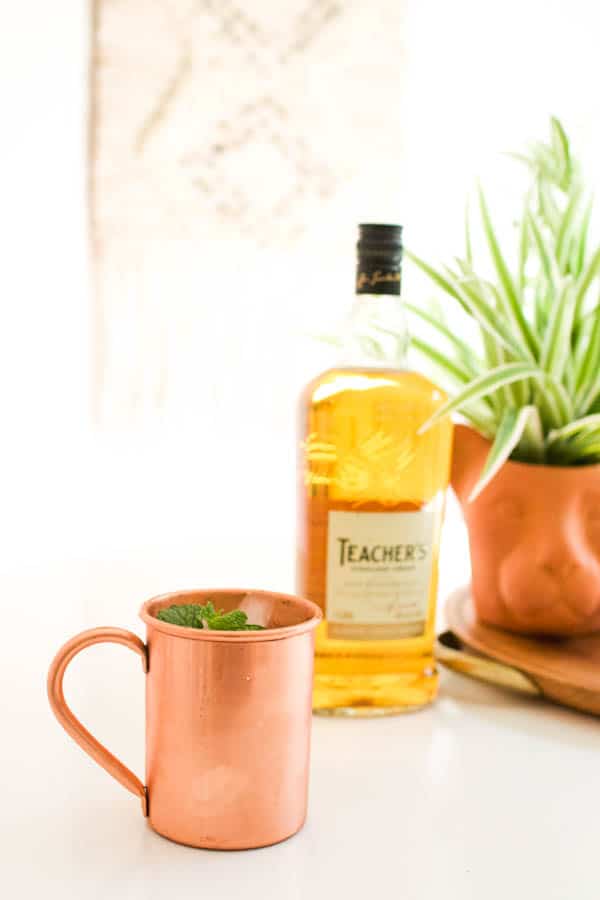 A copper mug on a table next to a bottle of scotch.