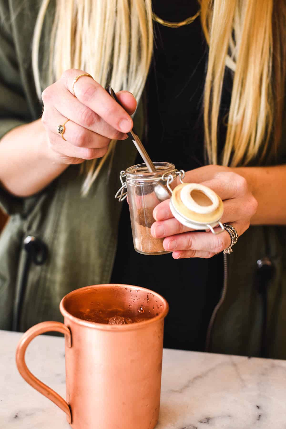 Woman measuring out some pumpkin pie spice from a jar.