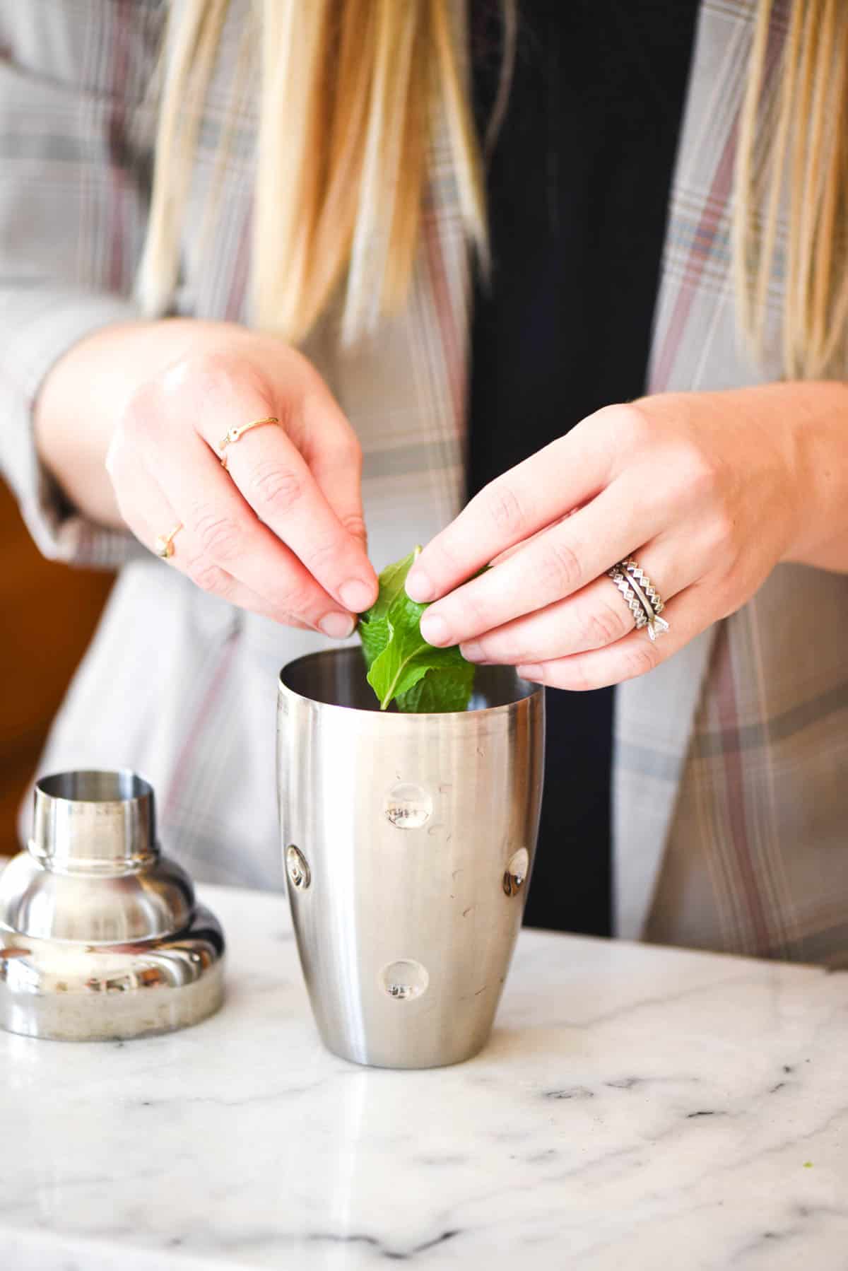Woman adding fresh mint to a cocktail shaker.