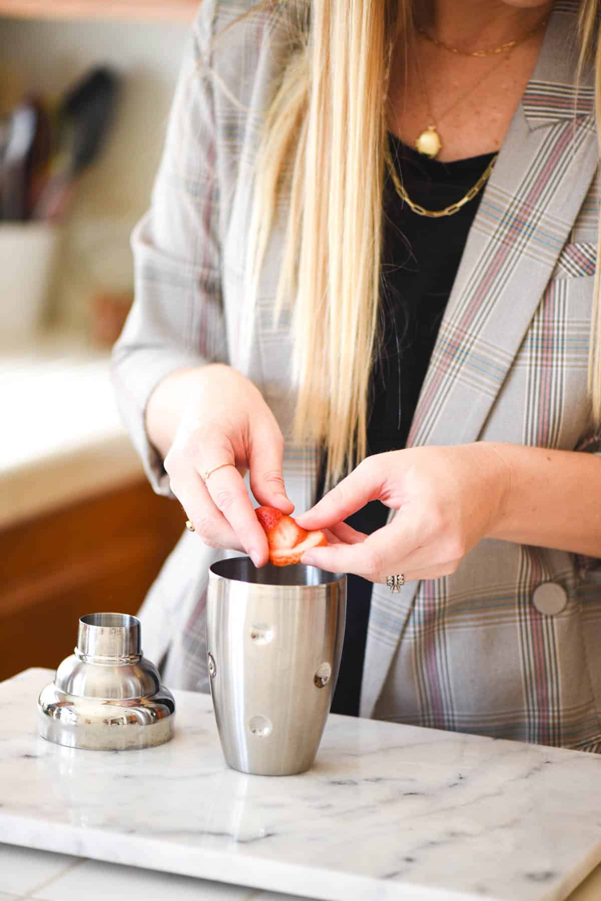 Woman adding fresh strawberries to a cocktail shaker.