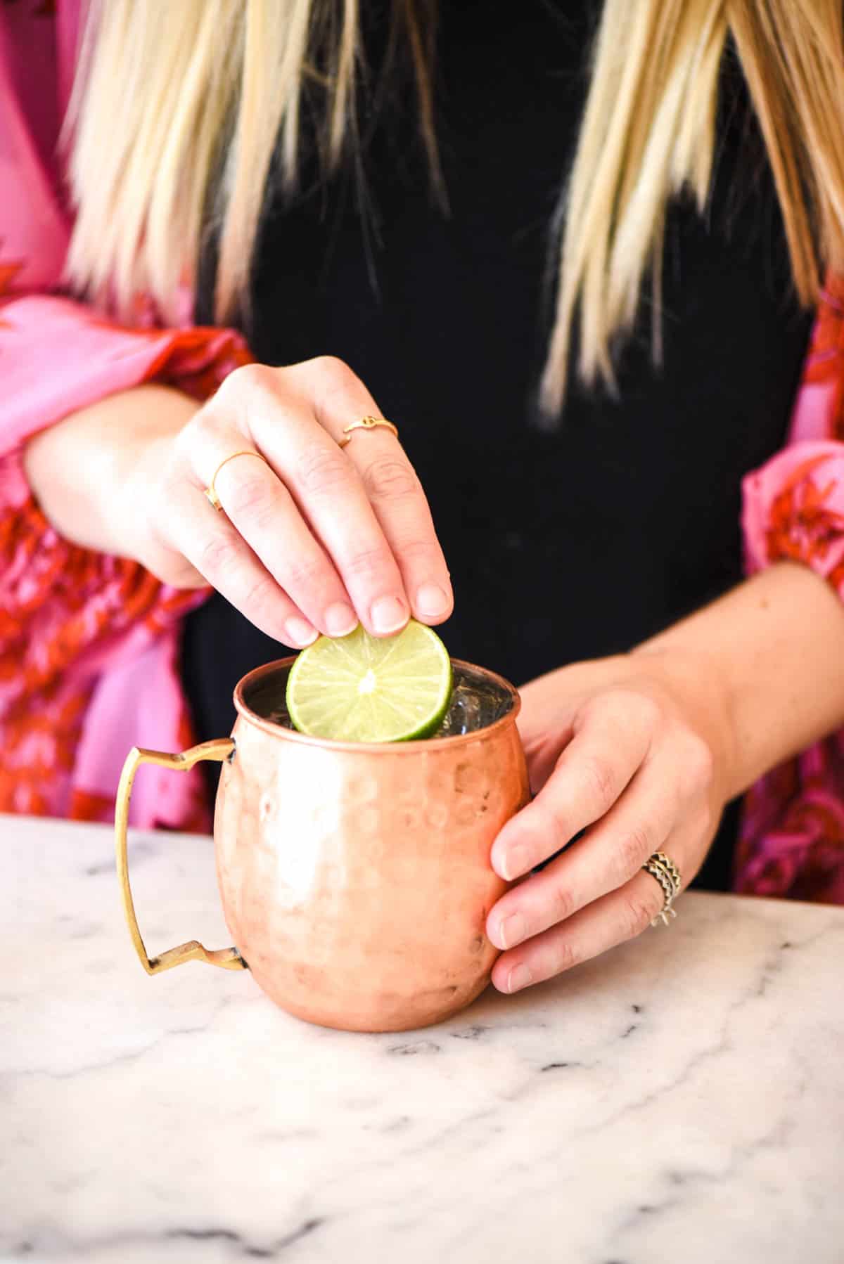 Woman adding a lime slice to the top of a cocktail in a copper mug.