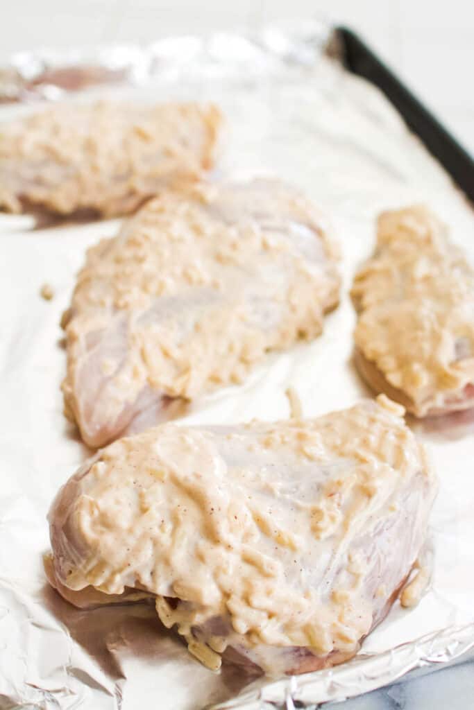 Close up of chicken breasts on a cookie sheet coated in mayo.