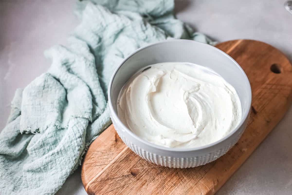 Close up of frosting in a bowl on a wooden cutting board.