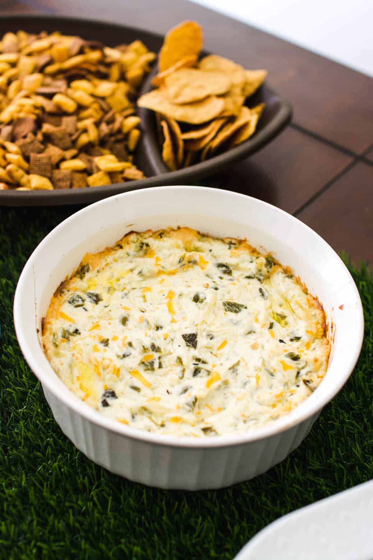 Cream cheese dip in a baking dish on a table next to a platter of chips.