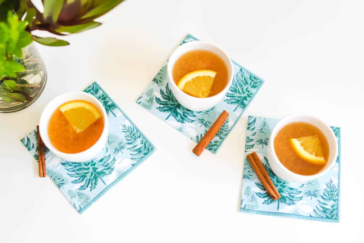 Overhead shot of small white mugs on a table with hot apple cider.